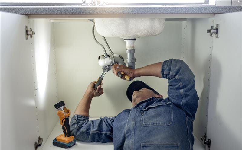 Plumber repairing pipes beneath a bathroom sink in Broomfield