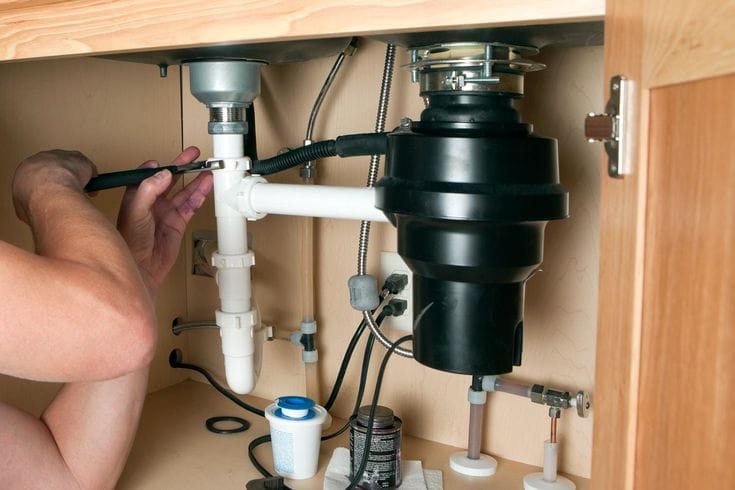 Plumber installing a garbage disposal beneath a kitchen sink in Broomfield