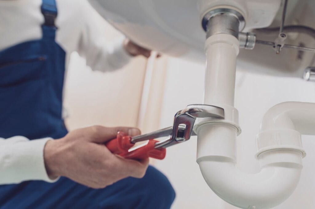 Plumber repairing a white drain pipe beneath a sink in Broomfield