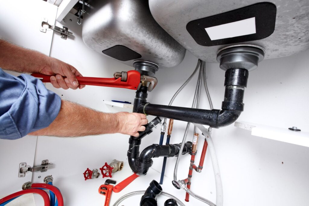 Plumber repairing drain pipes beneath a kitchen sink in Broomfield